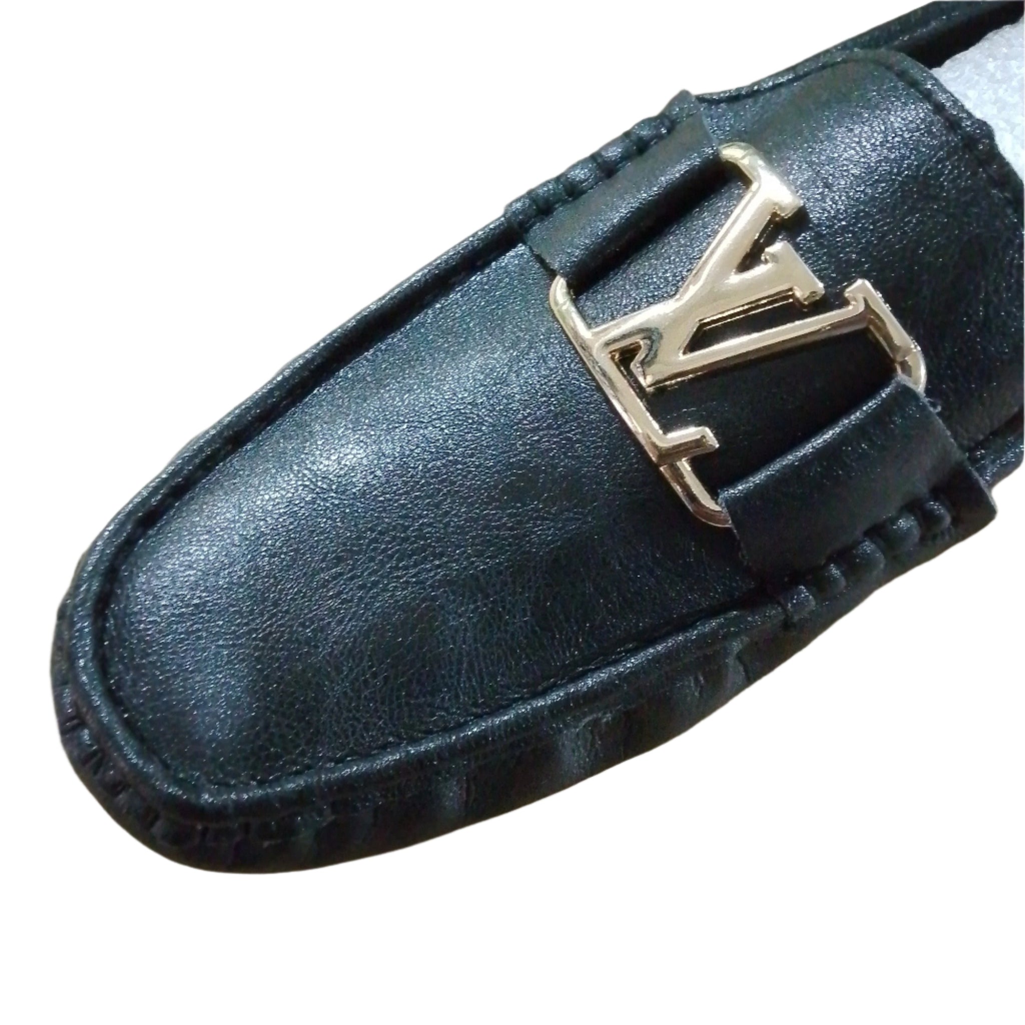 A single black loafer casual shoe with a metallic embellishment on the vamp, viewed from the side on a wooden floor background.